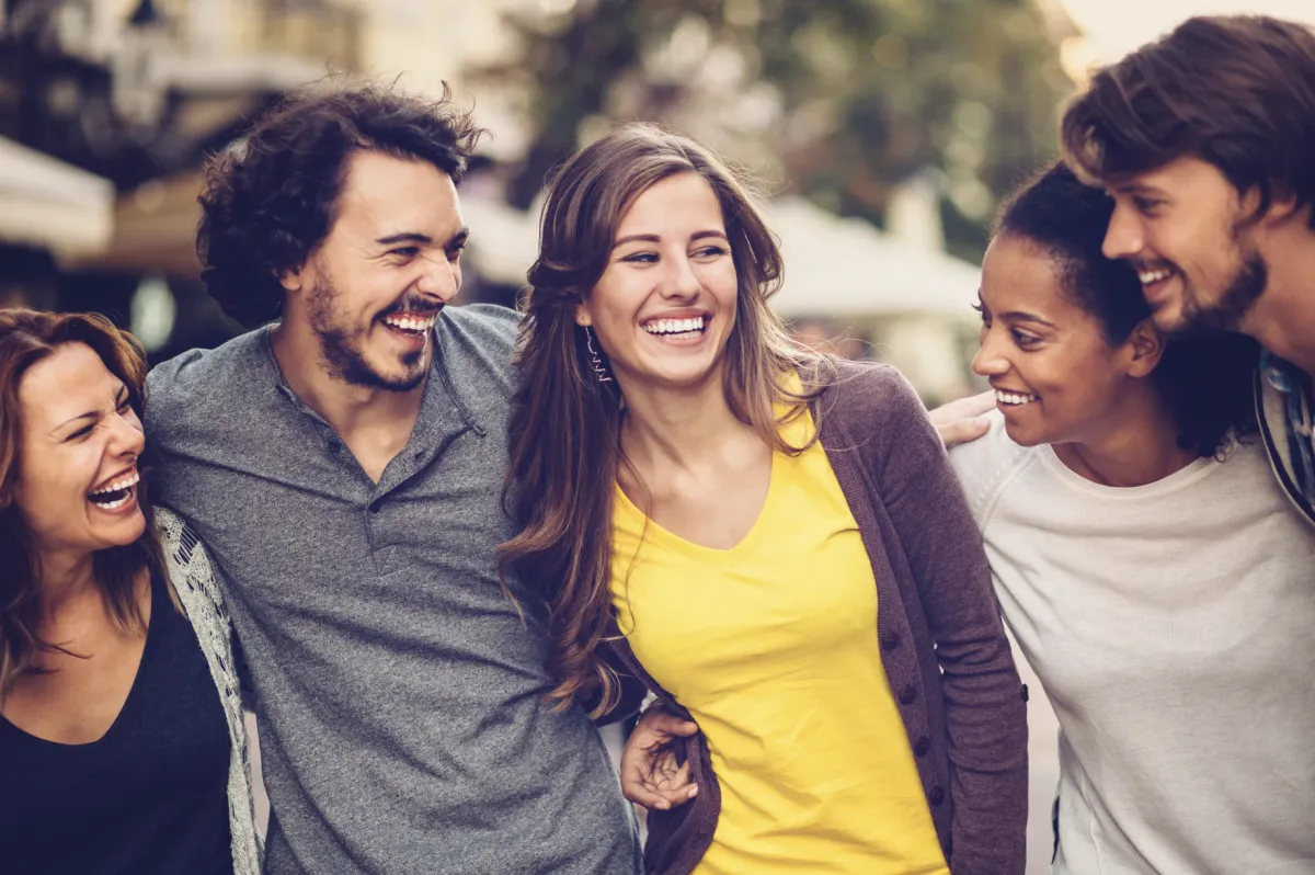 5 young adults smiling together arm in arm