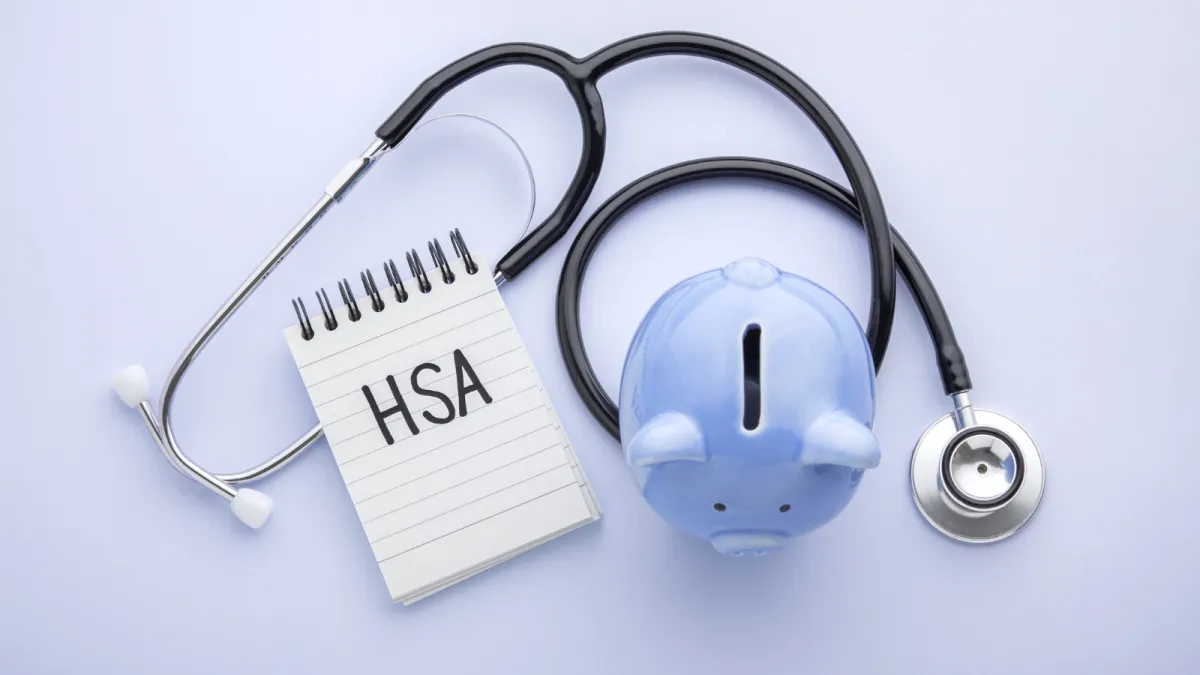 Blue piggy bank with a doctors stethoscope and notepad labeled HSA