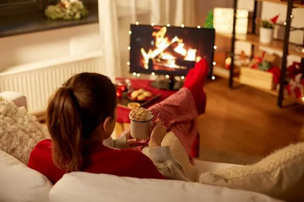 cozy woman watching a fireplace on TV drinking hot chocolate