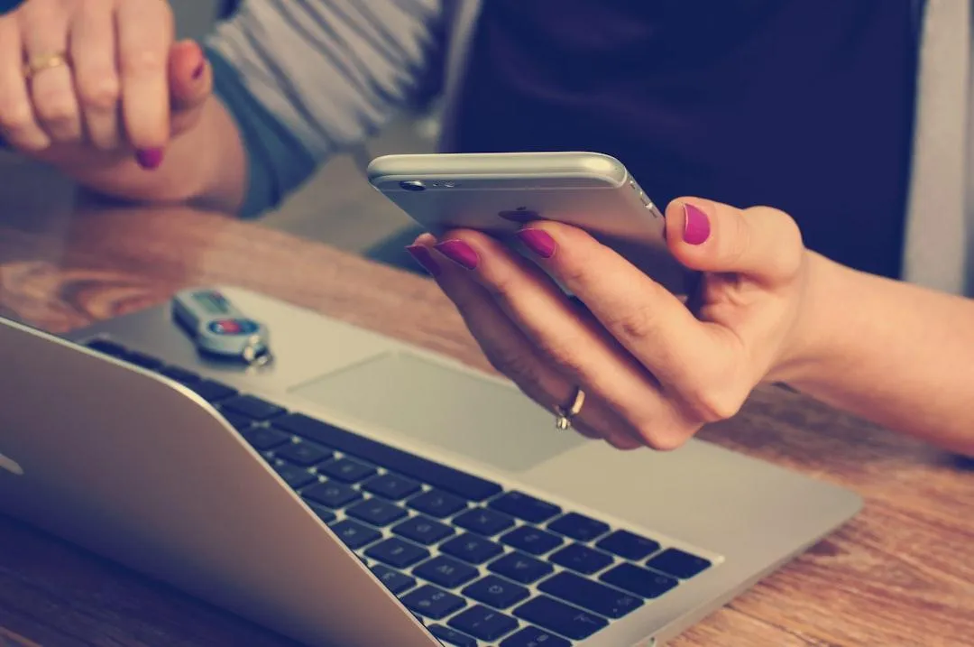 person holding phone next to laptop computer