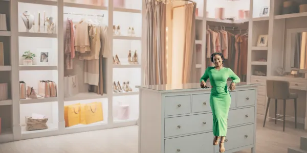 A professional organizer standing confidently in a beautifully designed luxury closet with neatly arranged clothing, accessories, and soft lighting showcasing an elegant, organized space.