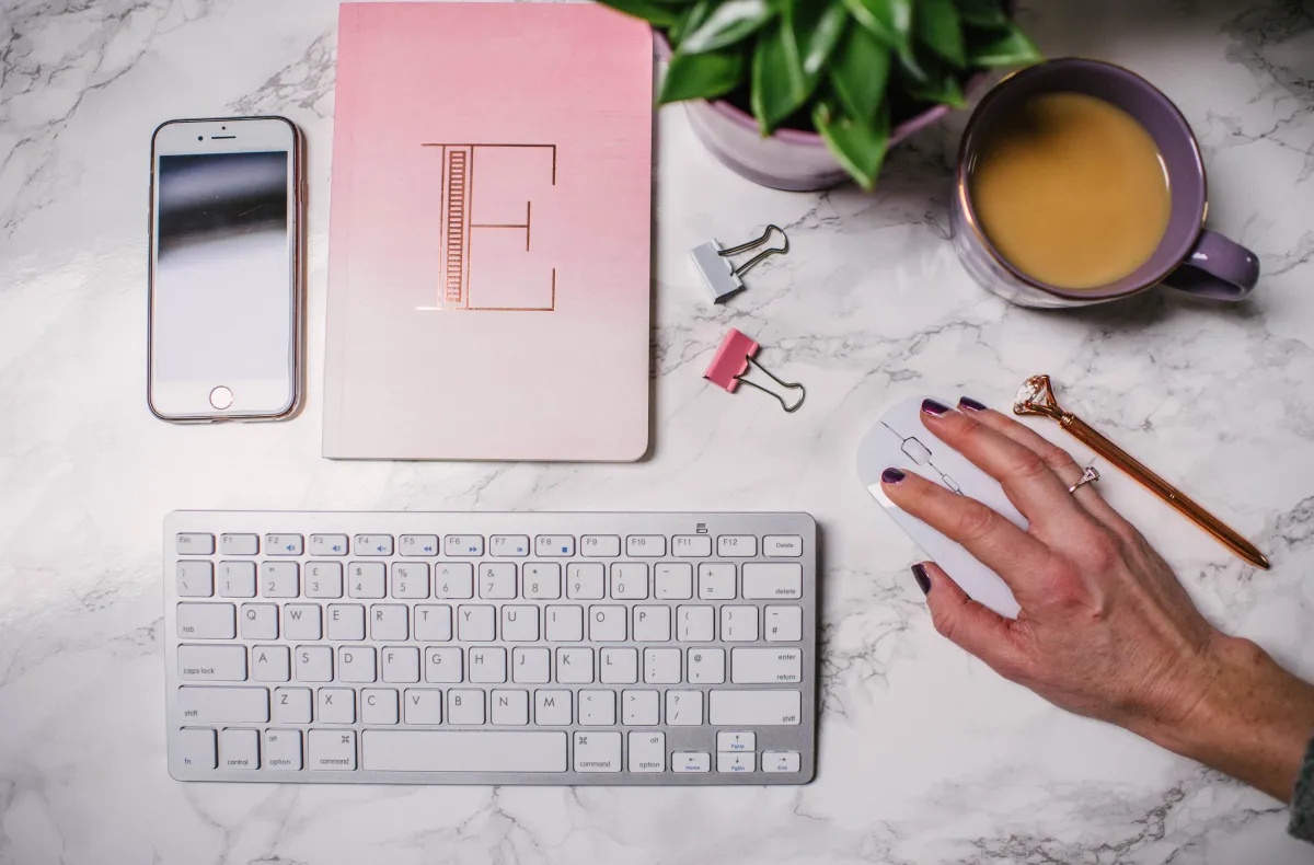 Keyboard, iPhone, hand over a mouse and notebook with the letter "E"