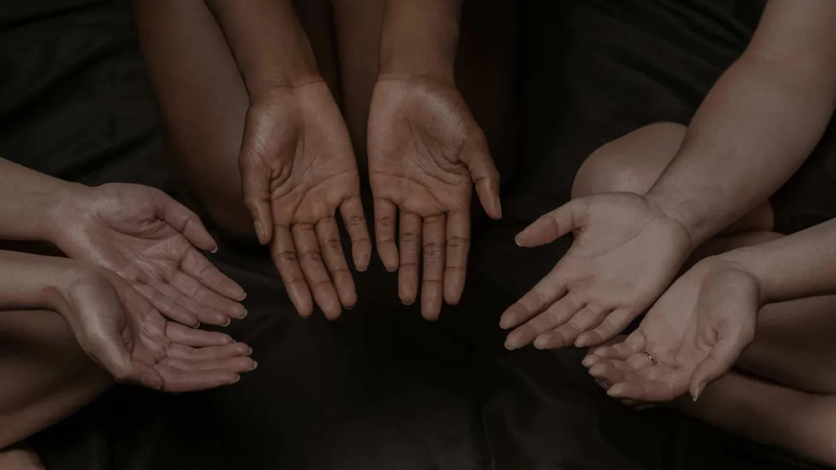 Four sets of hands extended in a gesture of giving, symbolizing community support and generosity.