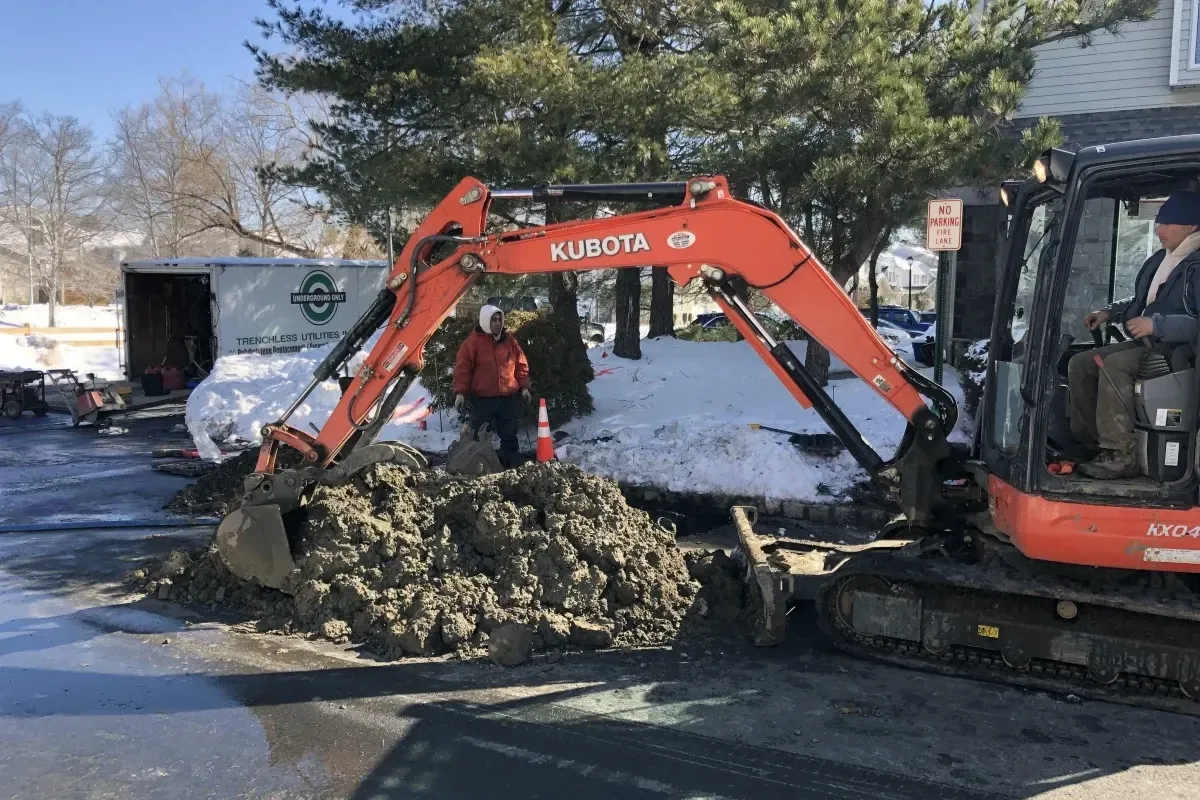 Excavation equipment and workers repairing a sewer line in a residential area during winter, showcasing professional trenchless plumbing and sewer repair services by American Underground Only.