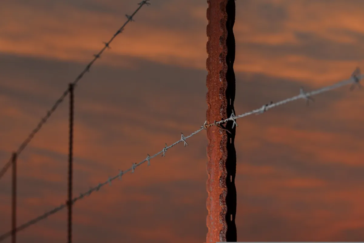 Close-up of a rusty barbed wire fence against a warm, sunset sky, symbolizing boundaries and protection.