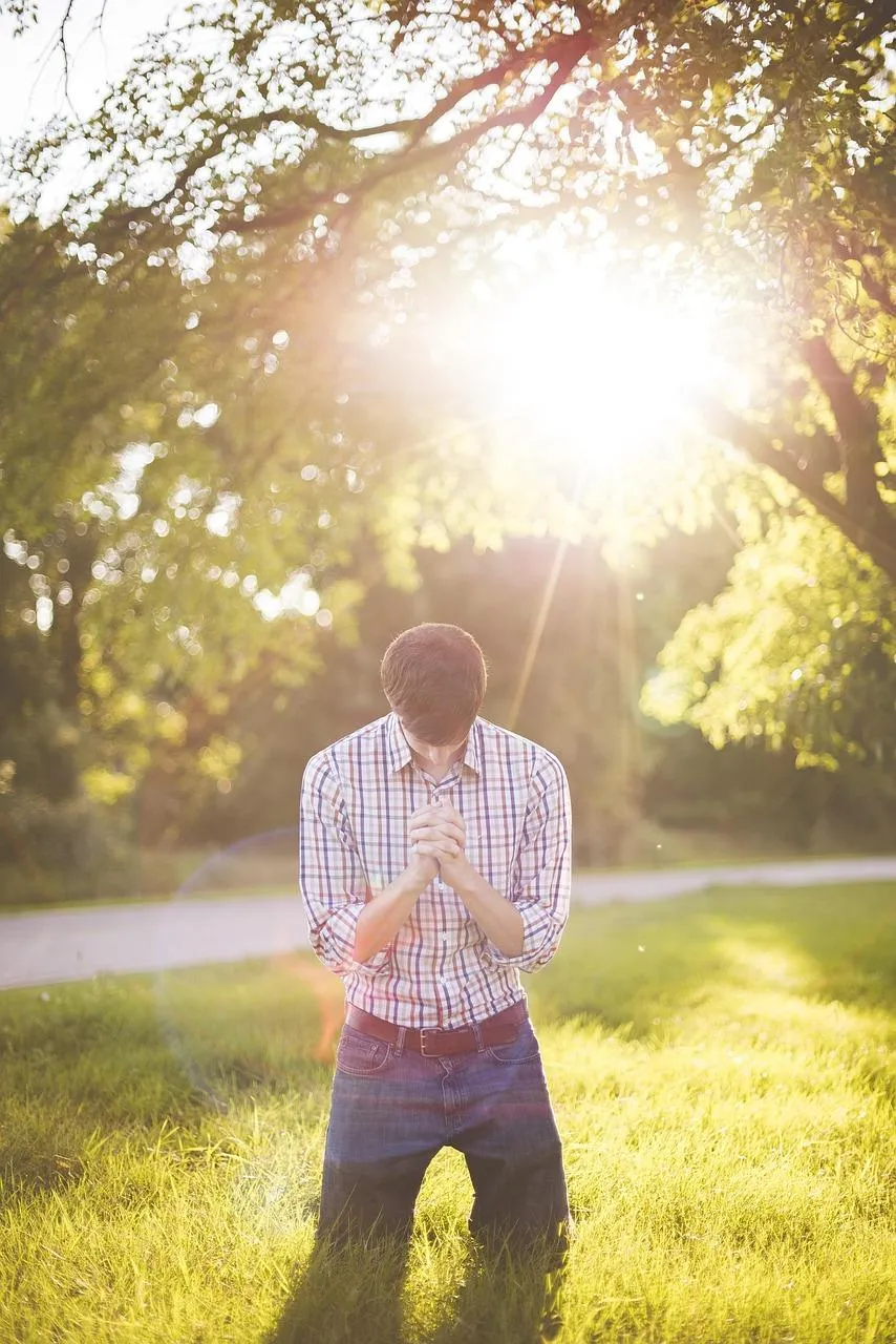 A person quietly praying with head bowed and hands folded, surrounded by soft natural light symbolizing silent, heartfelt prayers and God's unseen presence.