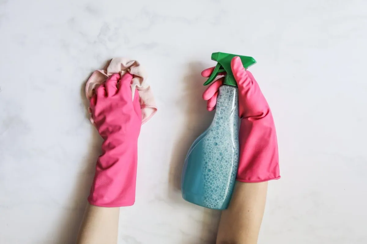 Eco-friendly home cleaning: Hands in pink rubber gloves cleaning a white surface with a cloth and spray bottle.