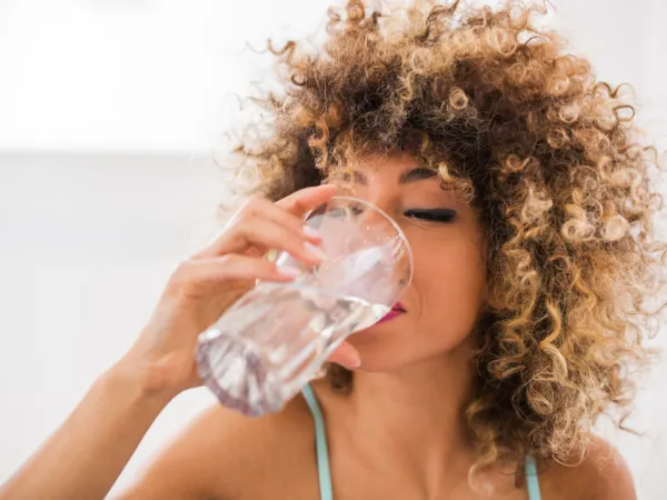 A women drinking a glass of tap water in aid of getting hydrated skin