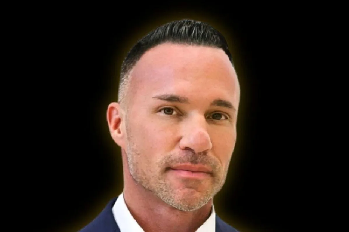 Marc Effron wearing a black suit with a white button down shirt that has the top button undone.