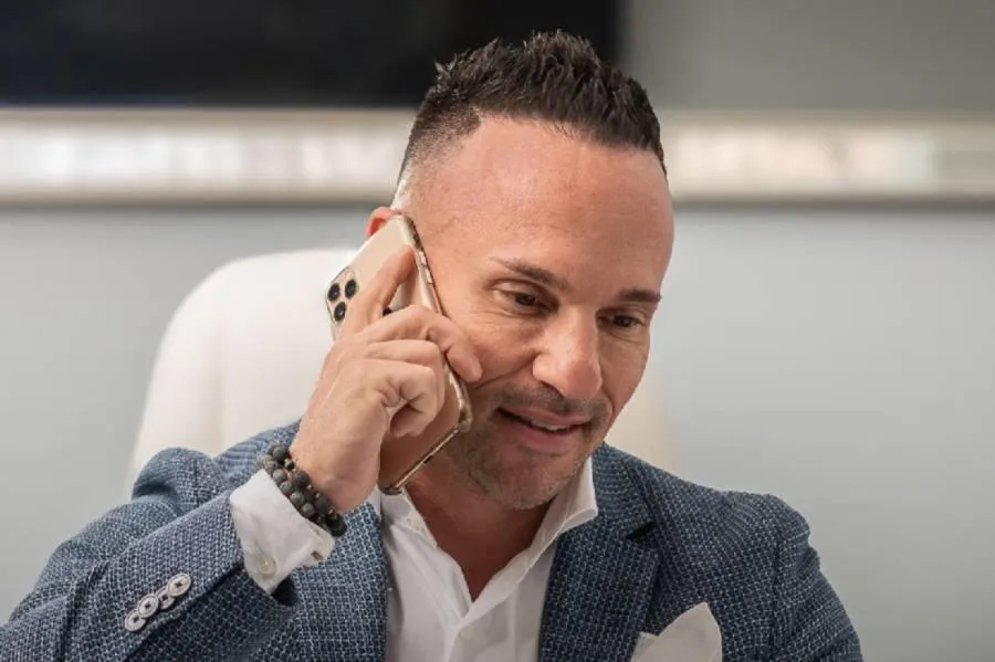 Marc Effron sitting in front of a window with green drapes, smiling because he can help people to create their leadership styles.