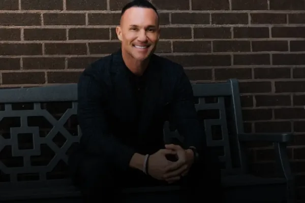 Marc Effron sitting on a bench in front of a brick wall and smiling.