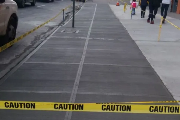 Full sidewalk repair in a commercial area with fresh broom-finished concrete, defined joints, and caution tape; visible pedestrian and vehicle traffic. Queens, New York
