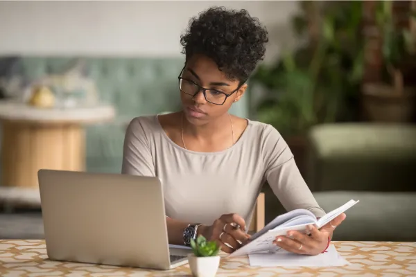 woman looking at a laptop while taking notes