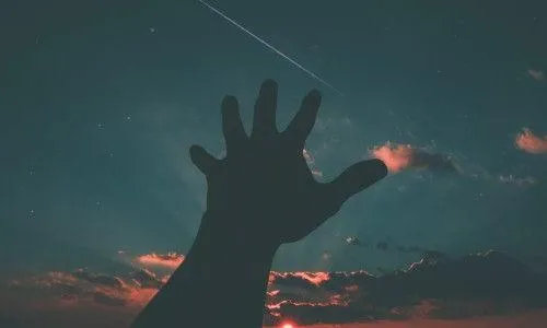 Silhouette of a hand against a night sky with a shooting star