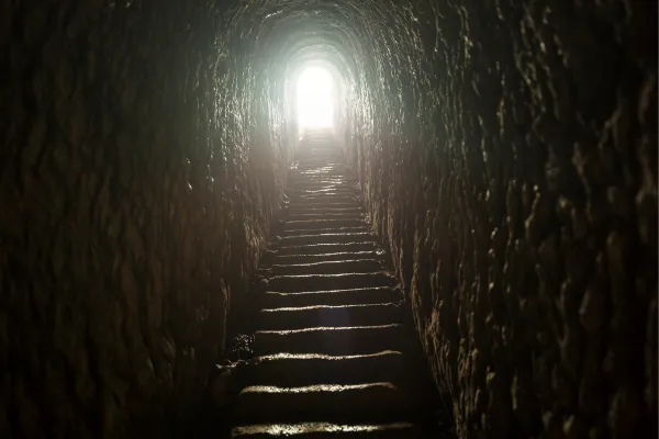 a dark tunnel with steps leading to a light at the end