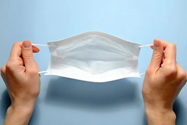 hands holding a surgical mask on a blue background