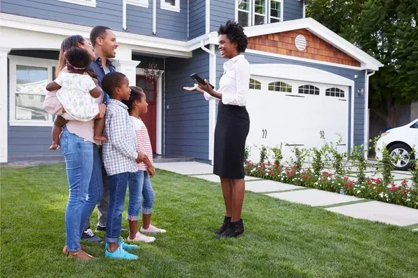 A picture of a real estate agent standing in front of a property that is for sale