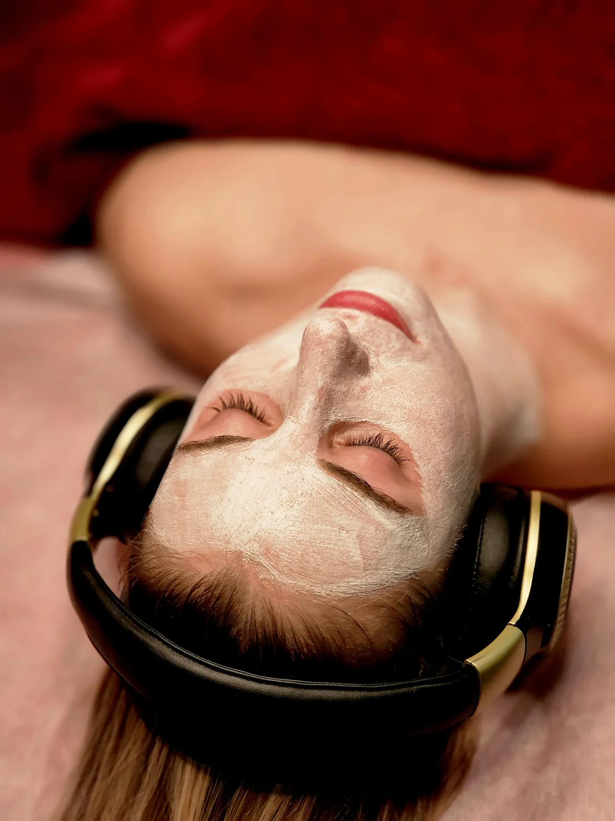 image of woman laying on treatment bed for a facial. she has a mask on and headphones listening to a meditation