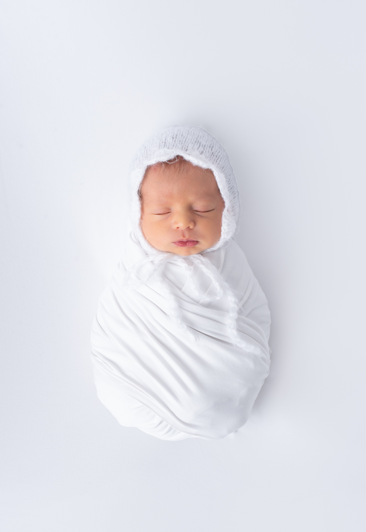 Newborn wrapped in white with a fuzzy bonnet
