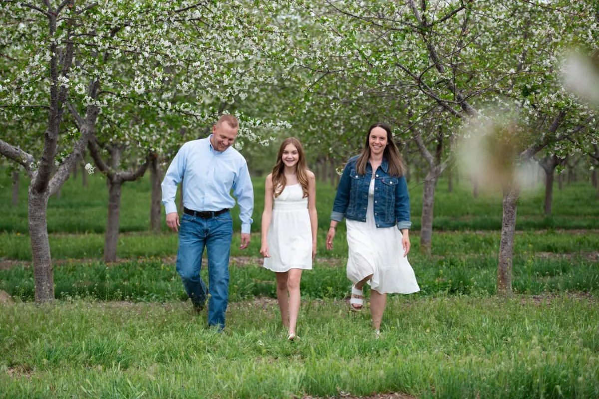 Family at Cherry Hill Farms walking in the flowering trees. Mom, Dad and daughter