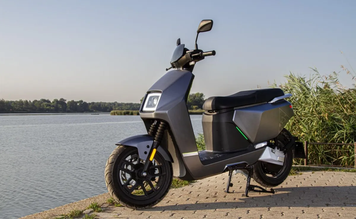Električni skuter VeloVoltage Titan v temno sivi barvi parkiran ob vodi, z izrazitim ostrim dizajnom in sodobnimi LED žarometi, pripravljen za dinamično mestno ali primestno vožnjo.