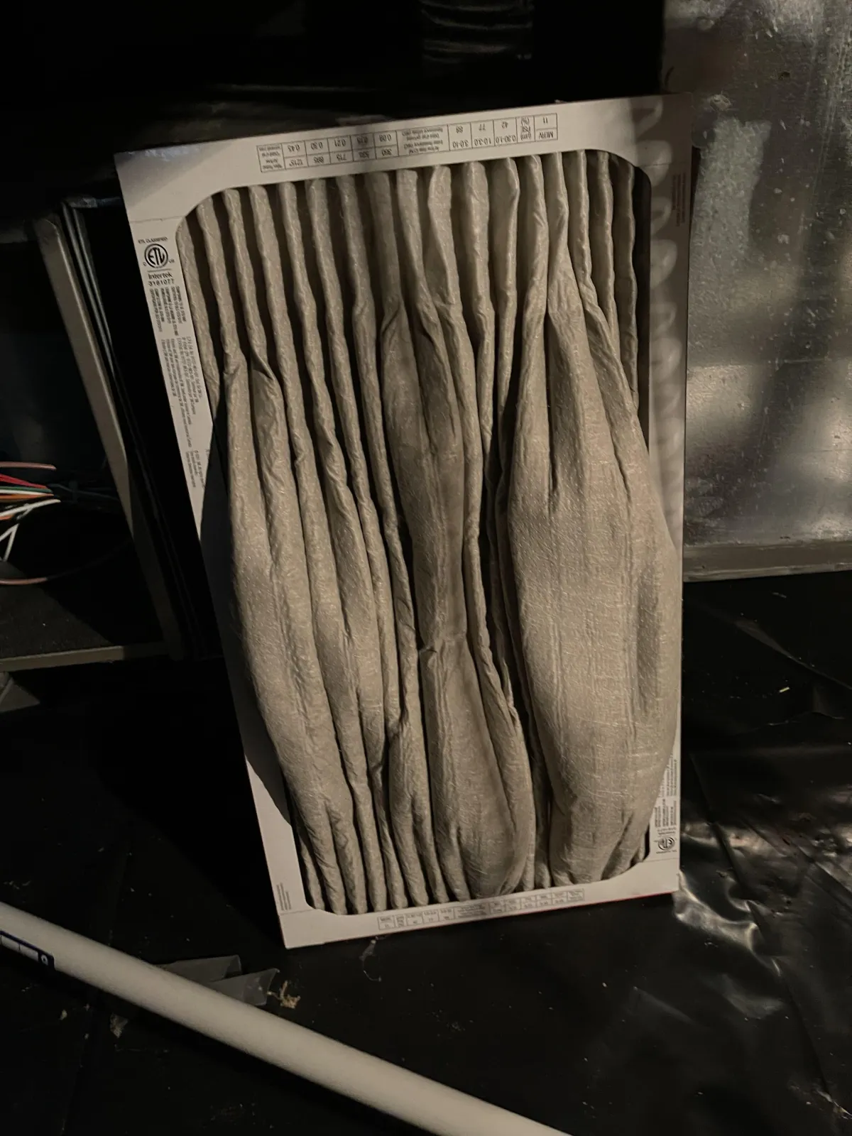 A heavily clogged and damaged HVAC filter, gray with accumulated dust and debris, showing signs of wear from airflow restriction.