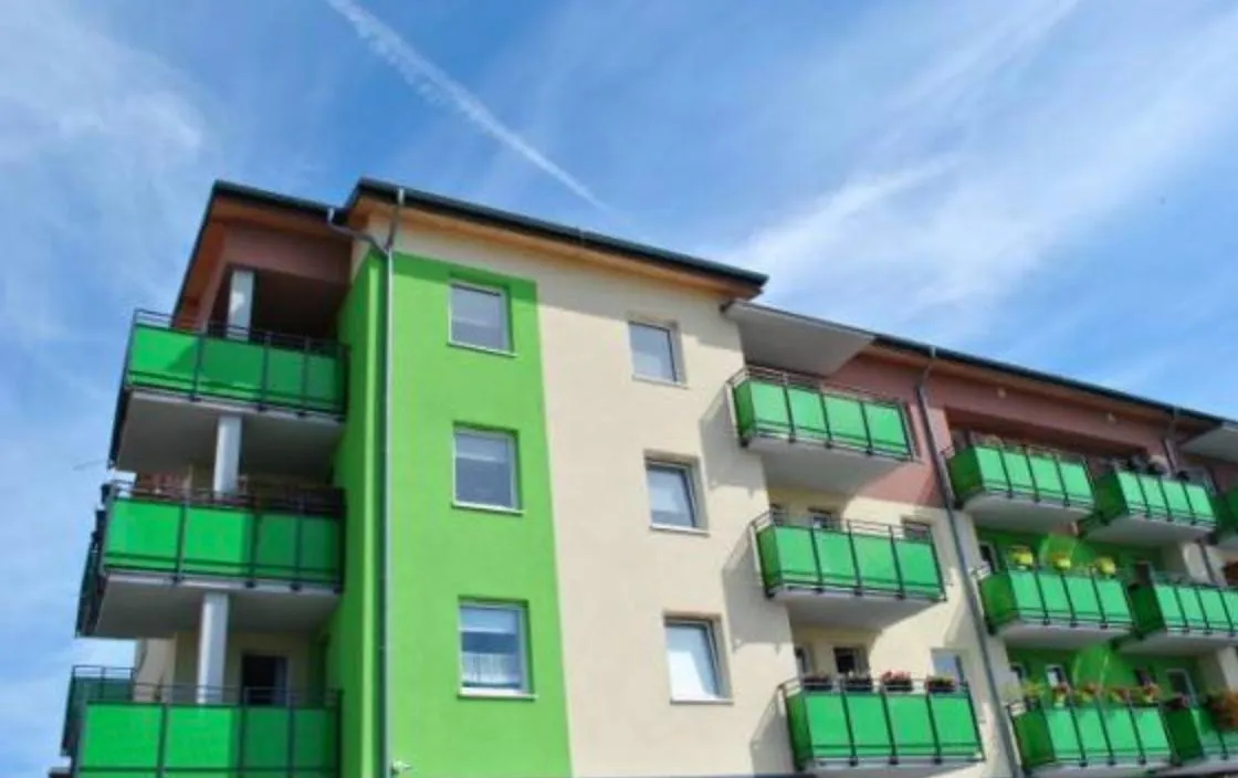 Green & beige apartment block in front of a blue sky with white wispy clouds