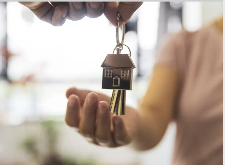 Person handing over a house-shaped keychain and keys to a new homeowner.