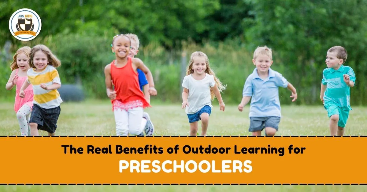 A group of preschool children joyfully running together outdoors on a grassy field with trees in the background. Text overlay reads ‘The Real Benefits of Outdoor Learning for Preschoolers’ with the Jus Kids International School logo in the top left corner.
