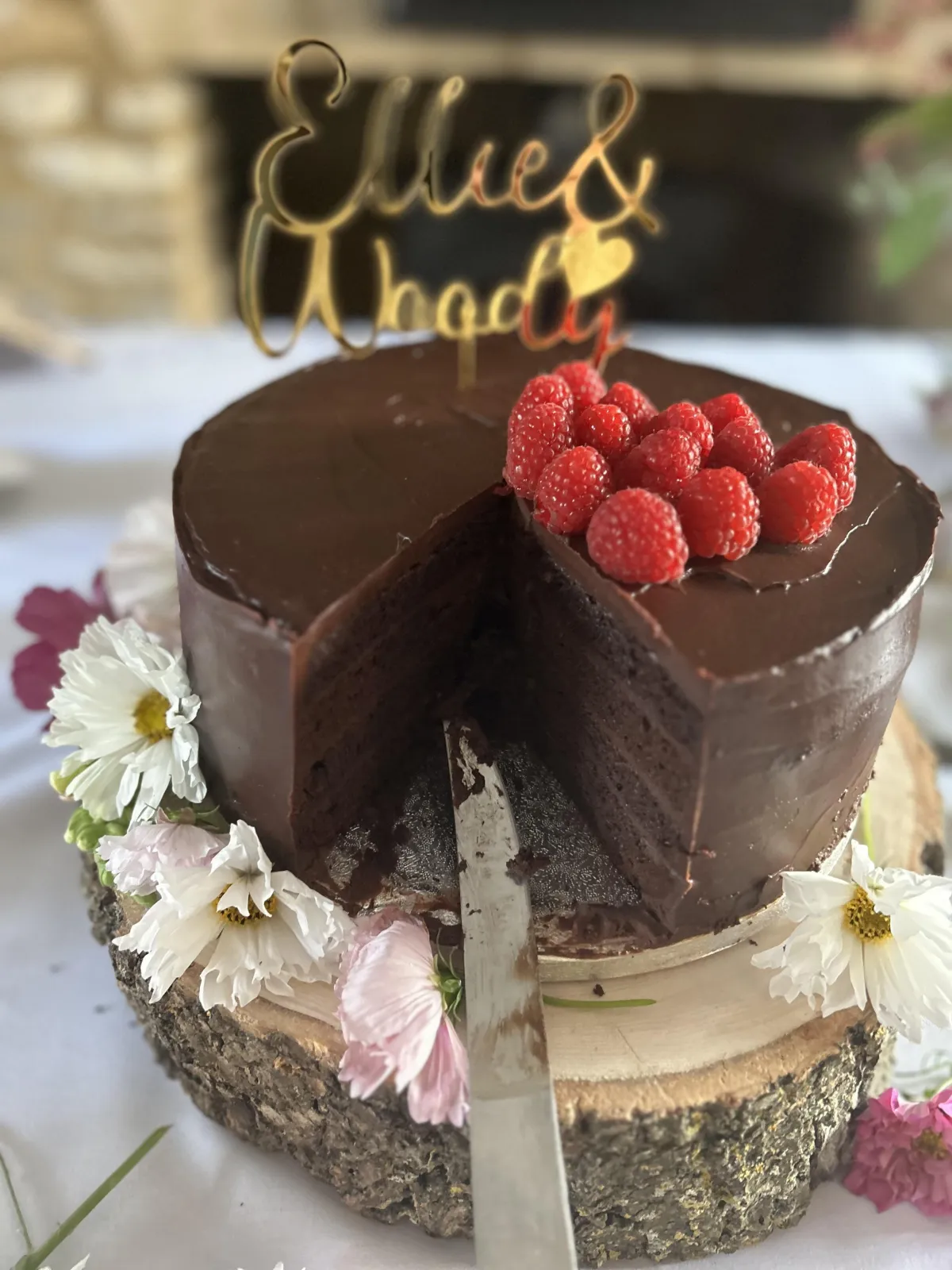 A beautiful chocolate ganache wedding cake, decorated with fresh flowers, raspberries, and a slice taken out by the bride and groom