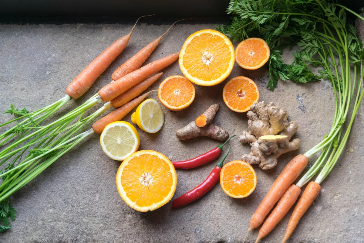 Carrots, lemons, oranges, ginger, cayenne, and turmeric are placed on a table.  The citrus and turmeric are sliced, showing a cross-section of the items.  These all help to boost immunity.