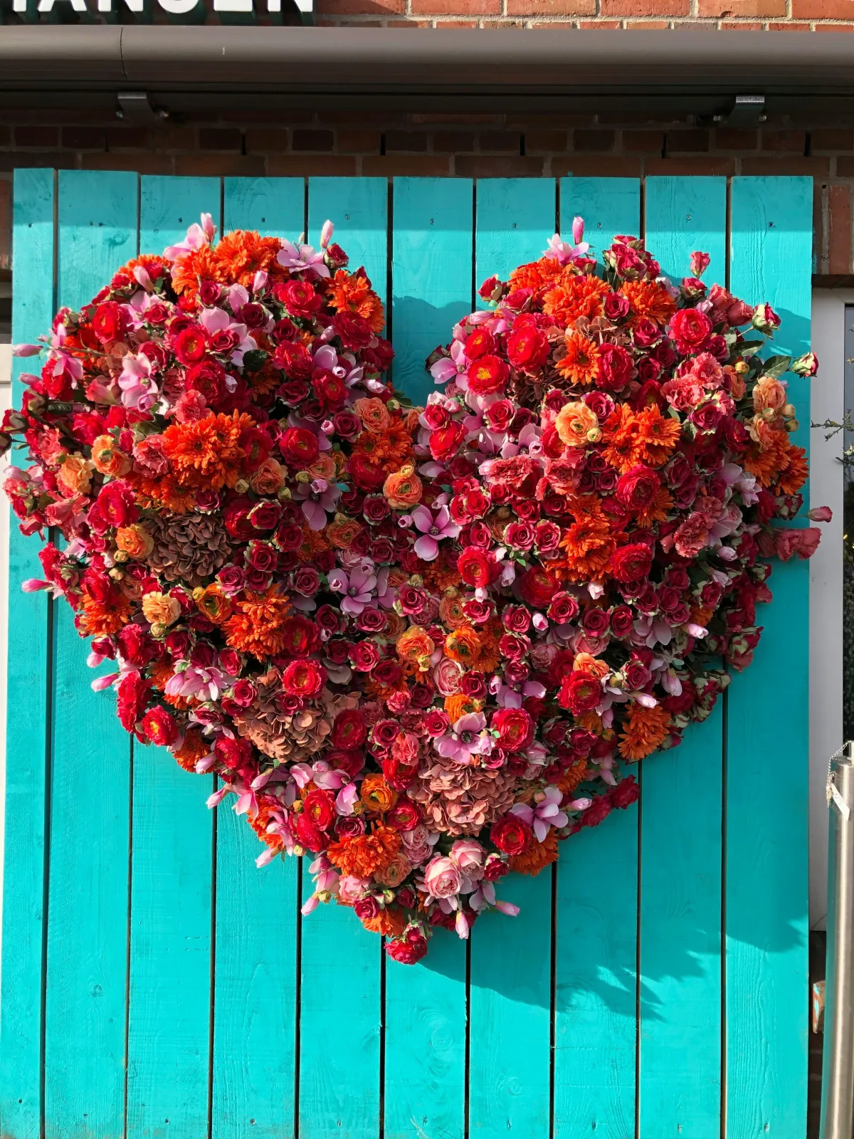 Image of red flowers in the shape of a heart.  The flowers are placed on a table made of turquoise-painted wooden slats.