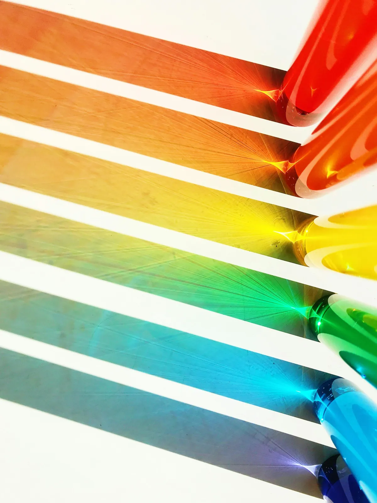 Multi-colored glass rods reflect their individual colors onto a white background.