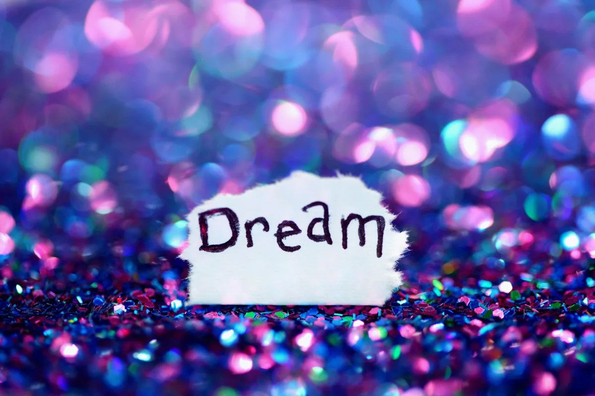 Purple and pink sparkles surround a piece of white paper with the word "Dream" on it