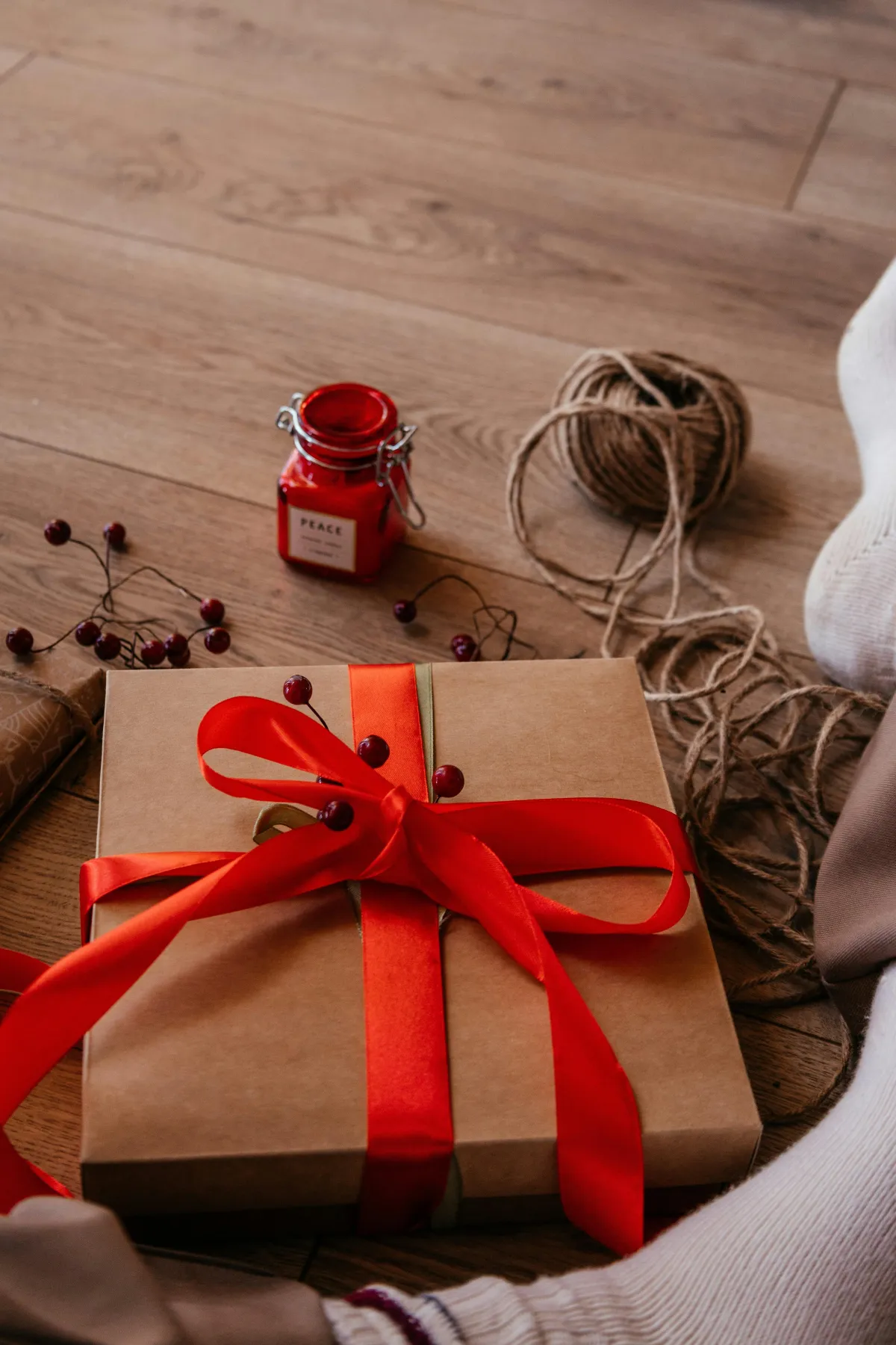 A present wrapped in brown paper with a red ribbon bow sits on a wooden floor