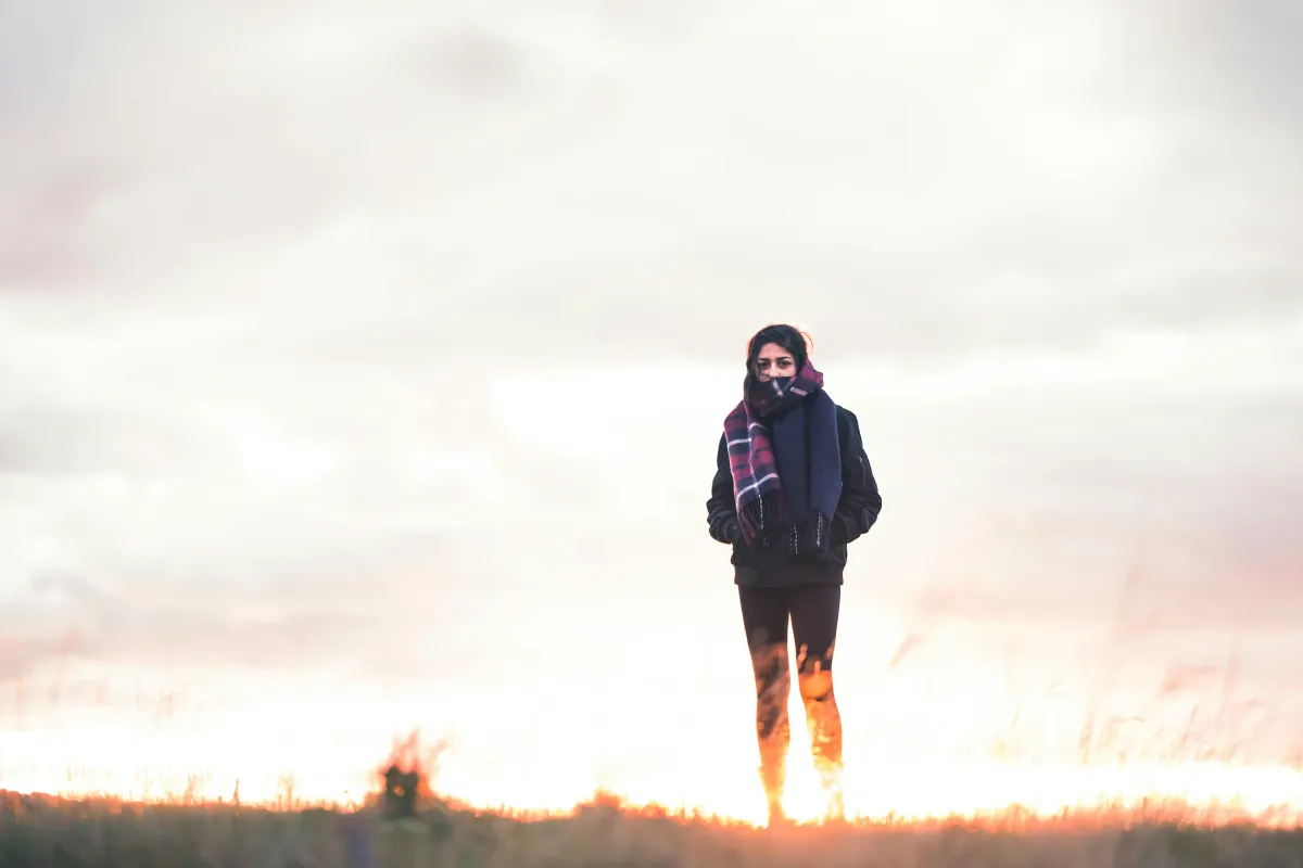 A woman is walking outside.  She's bundled up in jackets and scarves.