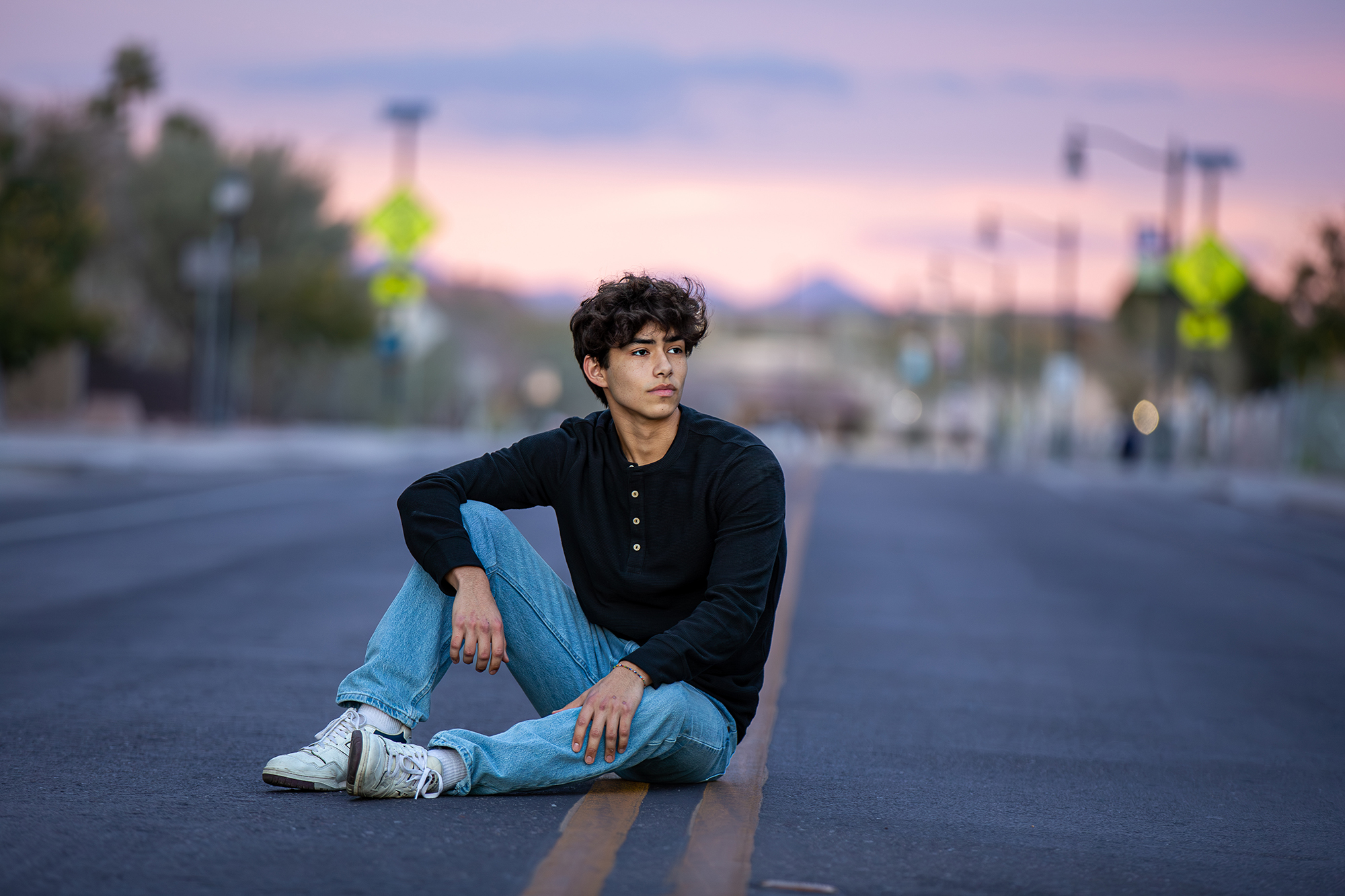 High school senior boy sitting on the road at sunset for a modern senior portrait in Gilbert Arizona.