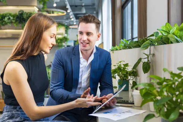  Man and woman reviewing a tablet and paperwork at a bright office with plants in the background.