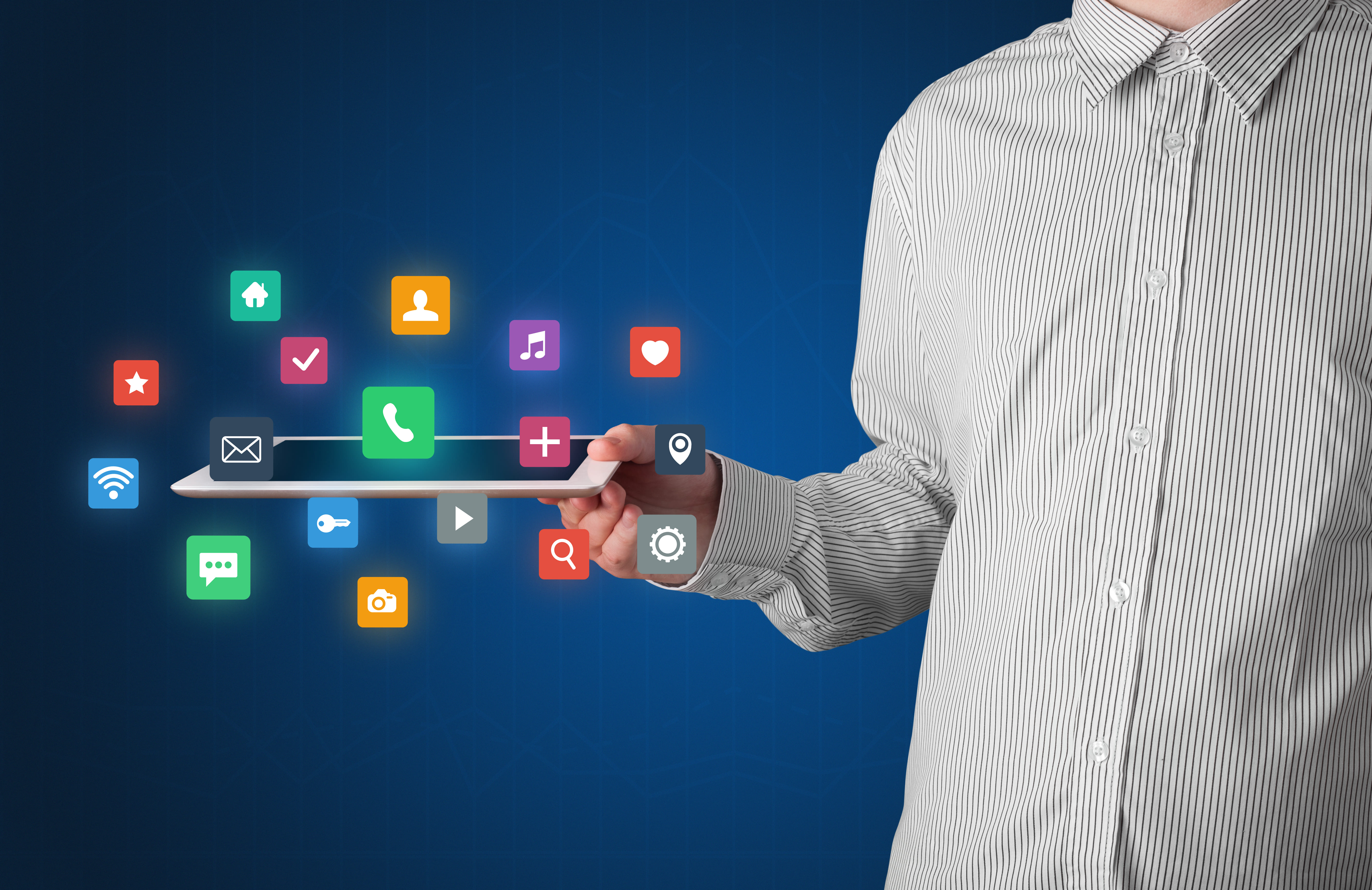 A person wearing a striped shirt holds a tablet in their hand, displaying a grid of colorful, glowing mobile application icons (including home, calendar, phone, music, heart, settings, and camera) floating above the screen against a dark blue background.