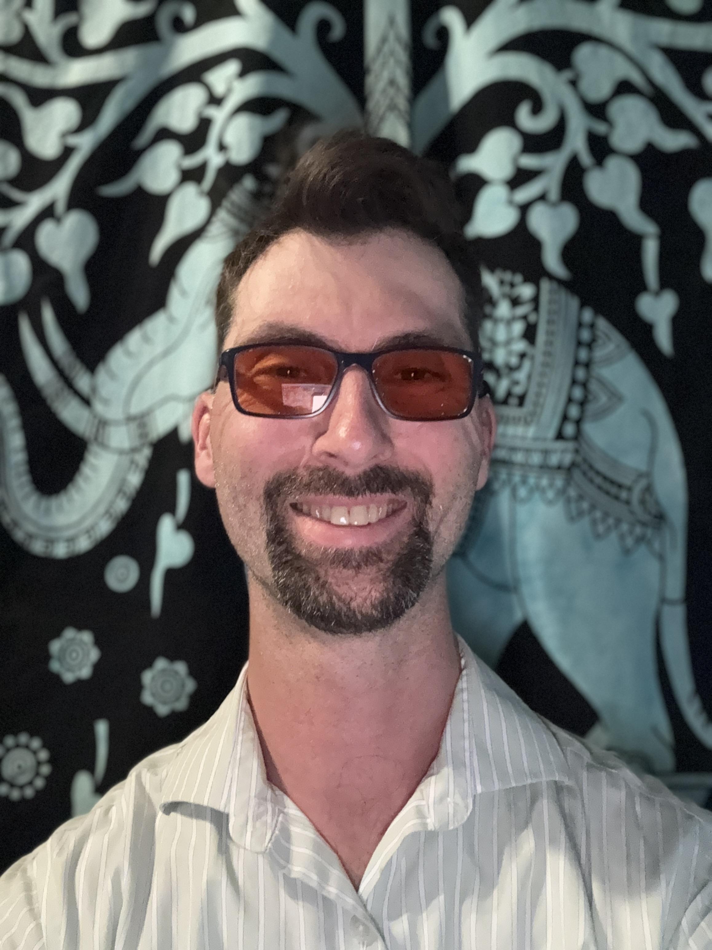 Kamiron Freeman wearing orange tinted glasses and a green dress shirt standing in front of a decorative elephant