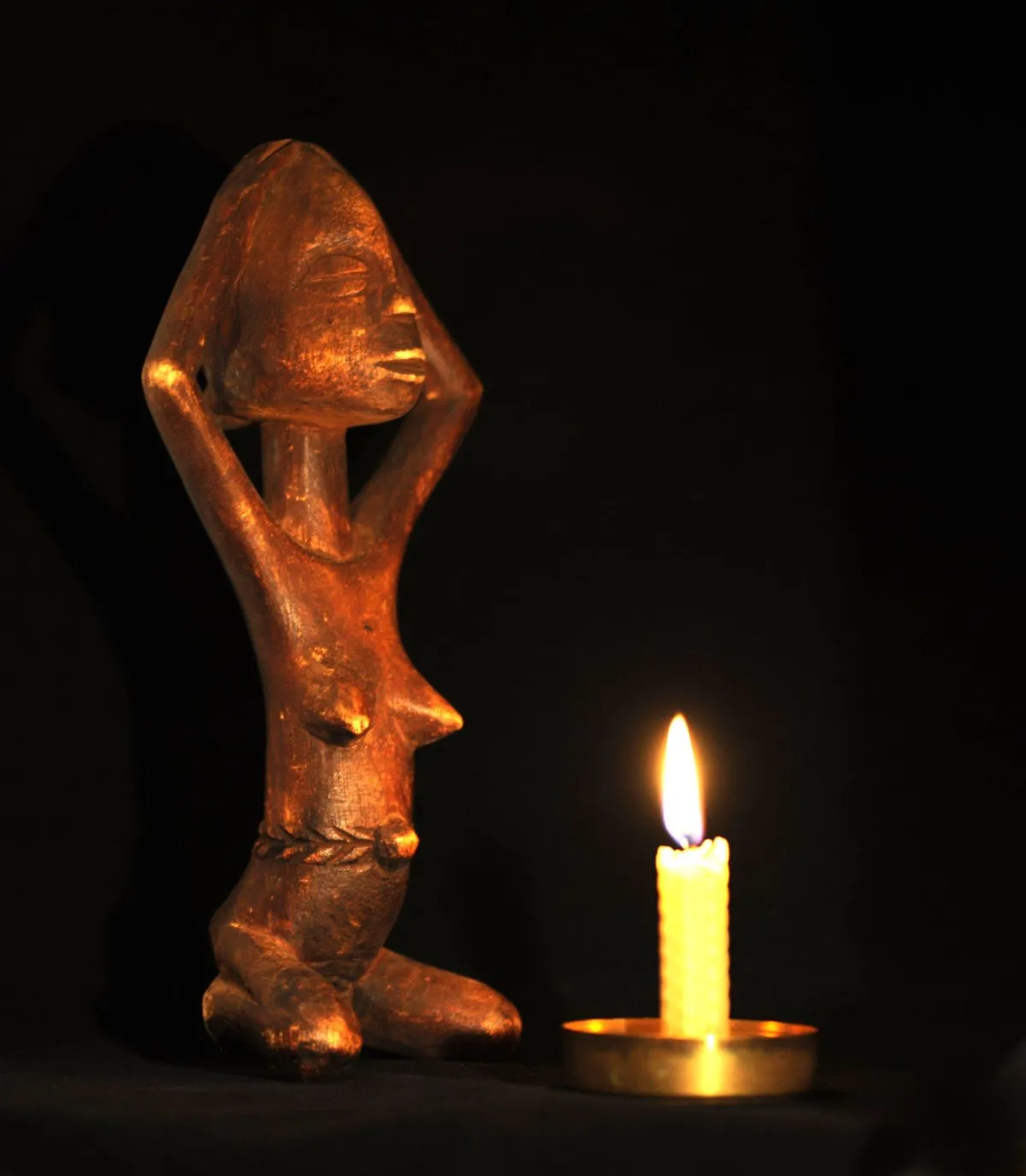 Female statuette kneeling in front of a lit candle.