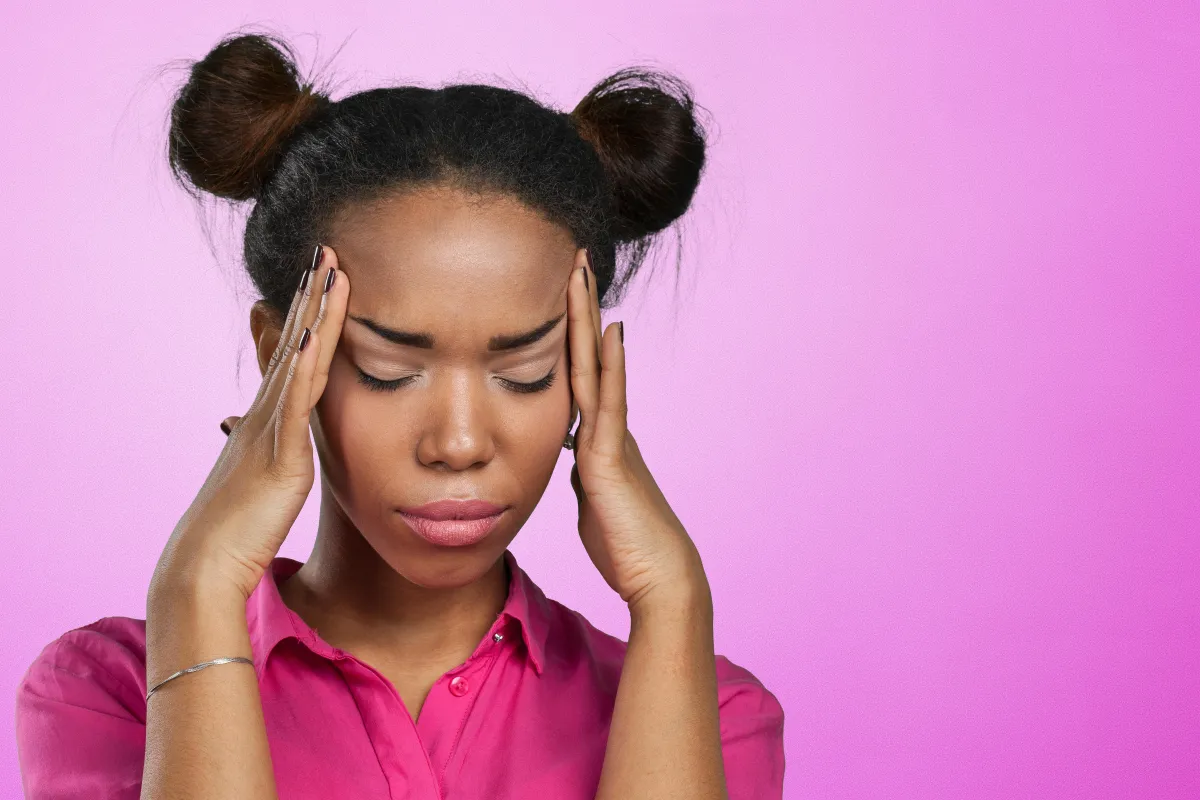 A woman holding her hands to her temples with her eyes shut tight seemingly in tension