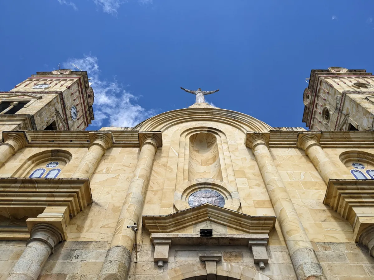 Jesus, arms raised heavenwards, stands on top of a beautiful yellow Colombian church