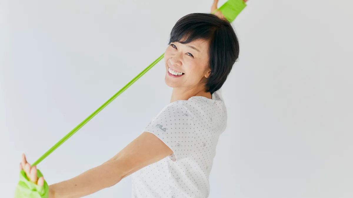 An older woman with a large smile gently stretches with an exercise band. 