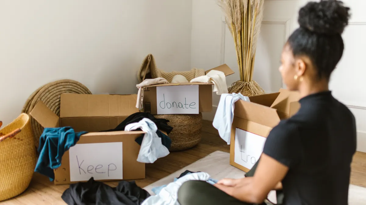 Woman sitting on the floor sorting her things into boxes labeled Keep, Donate and Trash. 