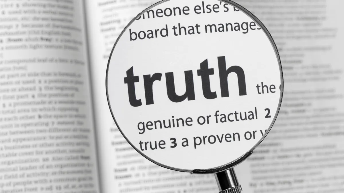 Dictionary with magnifying glass over the work truth. 