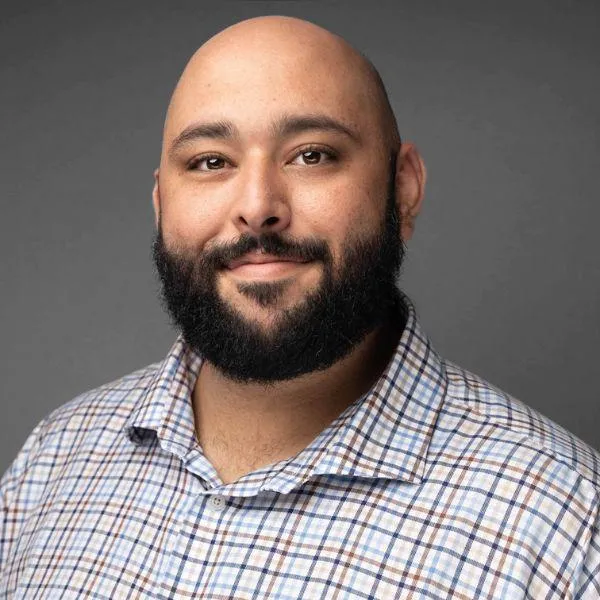 Professional headshot of a smiling Latino male business professional in a button-up shirt, taken for a social profile.