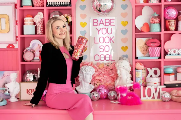 A woman wearing pink and black poses in a scene full of pink items