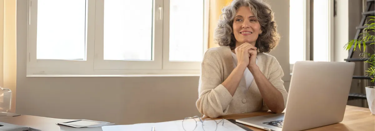 Midlife woman, taking a moment to relax and center, looking outside with soft natural light coming through the window.