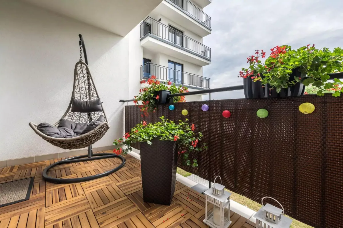 Cozy balcony decor with a comfortable hanging swing chair, vibrant flowering plants, and colorful lanterns, ideal for a stylish small outdoor retreat.